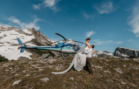 Groom lifts the bride with the helicopter at the background and rocky mountain with icecap.